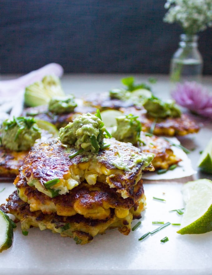 a stack of corn fritters with the last one bitten up to show the texture and a dollop of guacamole