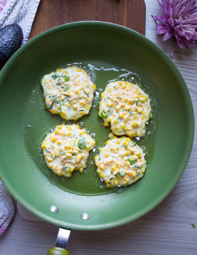 four corn fritters cooking in a hot skillet