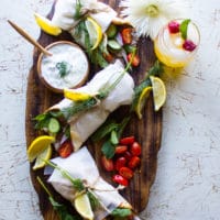 A platter of three gyros sandwiches with a bowl of tzatziki sauce and fresh tomatoes