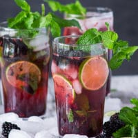 Close up of three cups of blackberry mojitos surrounded by ice