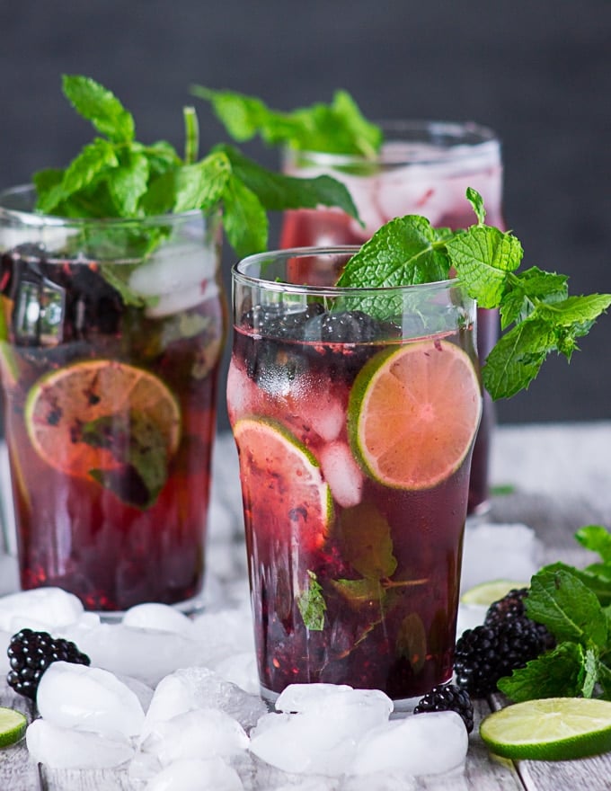 Close up of three cups of blackberry mojitos surrounded by ice