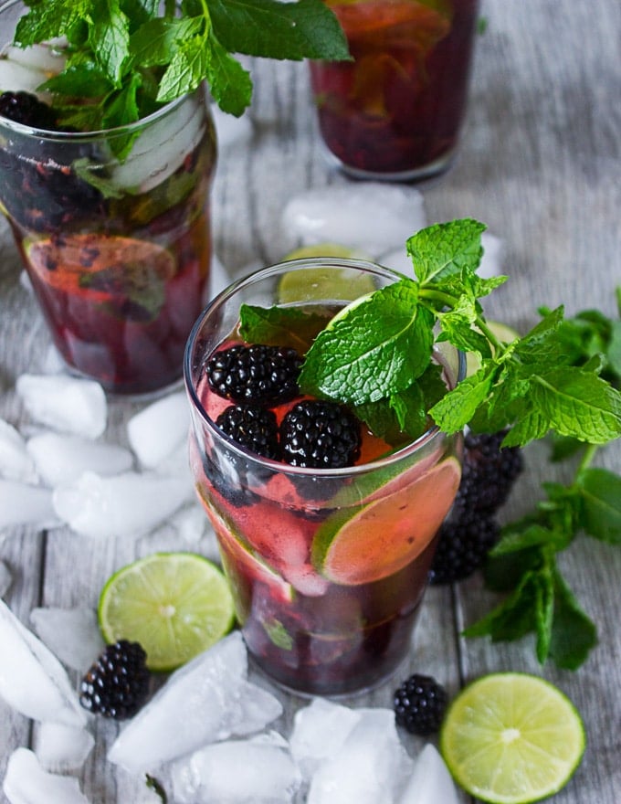 Three different cups of blackberry mojitos with different garnishes, such as blackberries, mint and lime slices