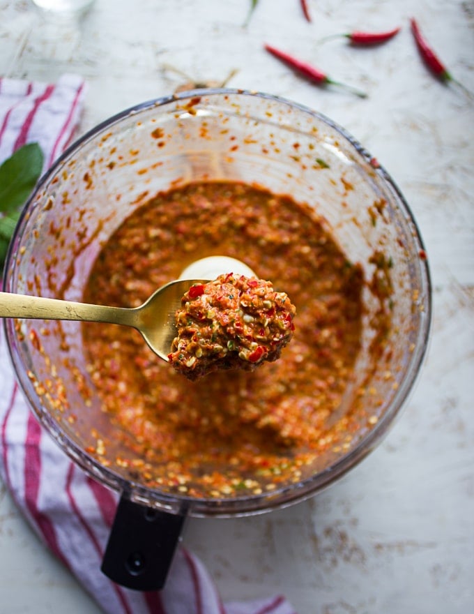 A spoon holding the chunky hot sauce over the food processor showing the final texture