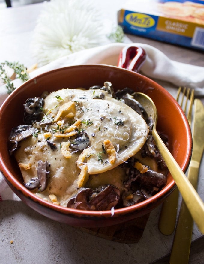 Side view of the finished pierogies in alfredo sauce with a spoon and fork, surrounded by a tea towel