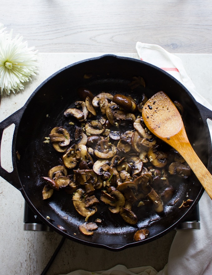 A large pan with the mushrooms and garlic sauteed together with a wooden spoon