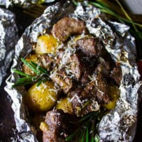 well cooked lamb and potatoes wrapped in foil packets and close up