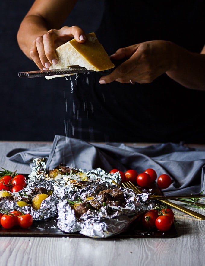 A hand grating Parmesan cheese over the ready foil packets