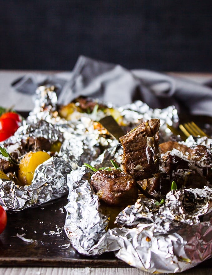 A fork holding a piece of cooked lamb from the foil packets