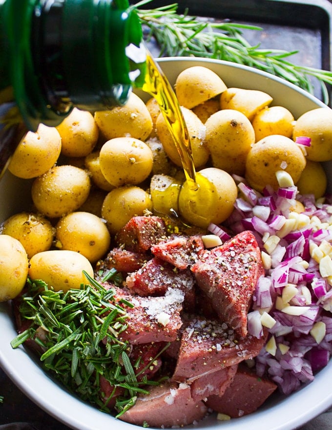 olive oil poured over the bowl of potatoes, lamb, onions and garlic