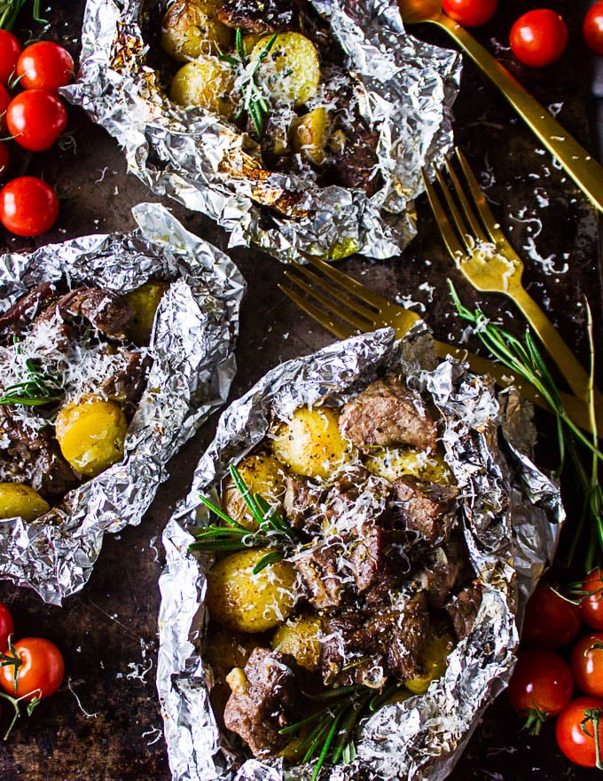 Two foil packets on the grill cooked and opened on the top to show the lamb and potatoes sprinkled with parmesan cheese and a golden fork on the side