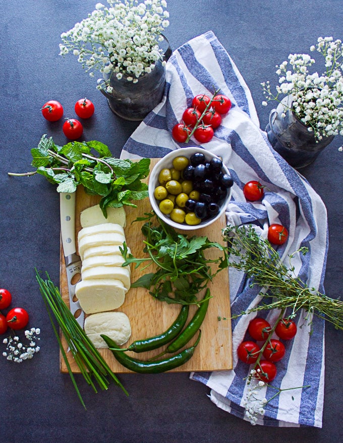 ingredients for the halloumi cheese salad on a cuttng board including olives, tomatoes, fresh mint