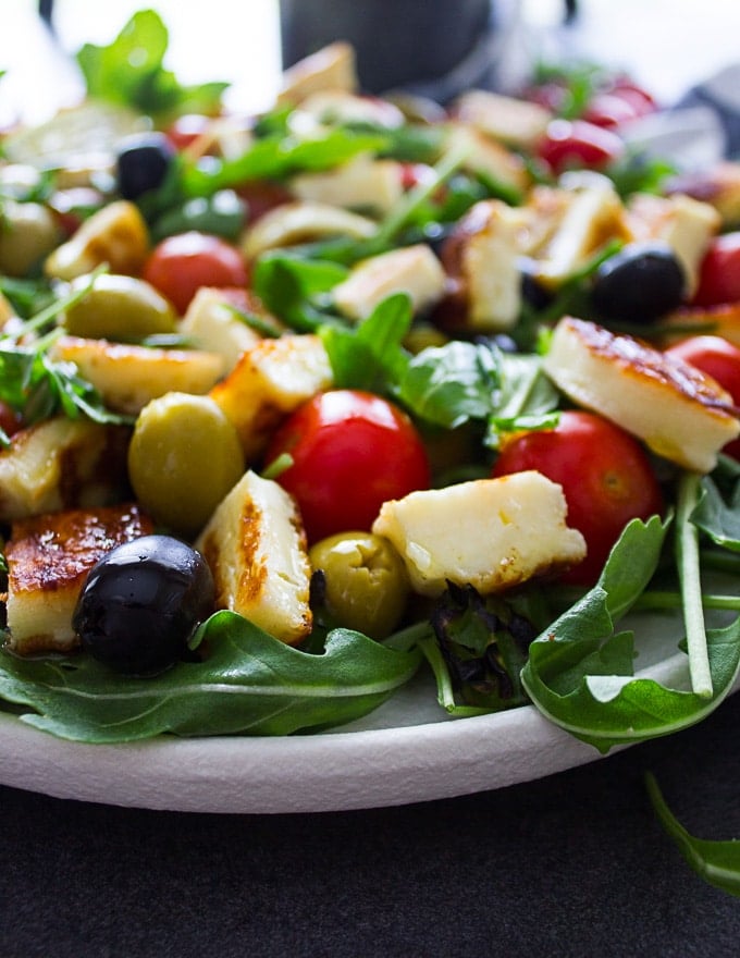 close up of the grilled halloumi and olives and tomatoes on a bed of arugula