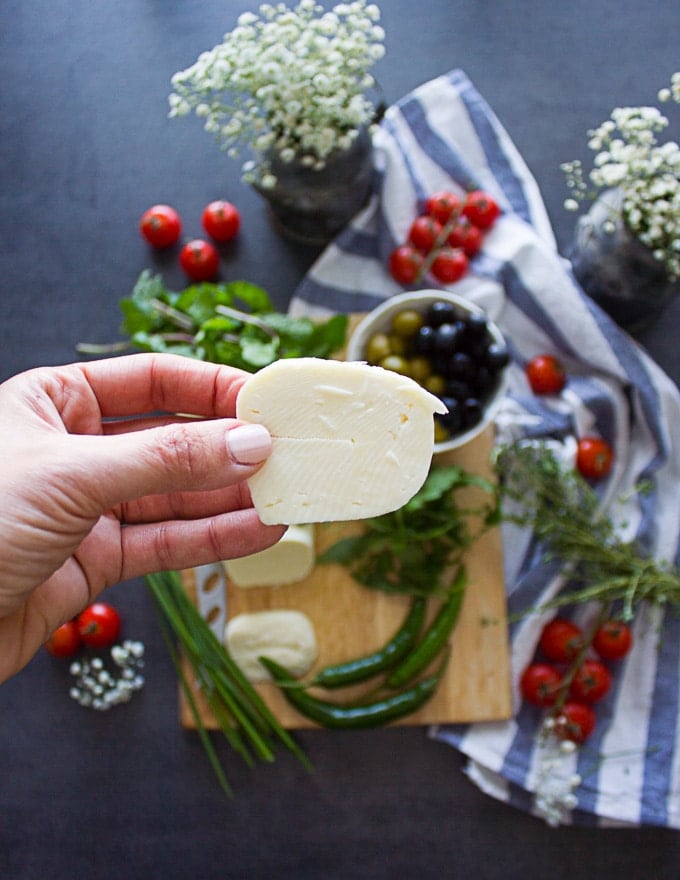 a hand holding a slice of halloumi cheese ready for grilling