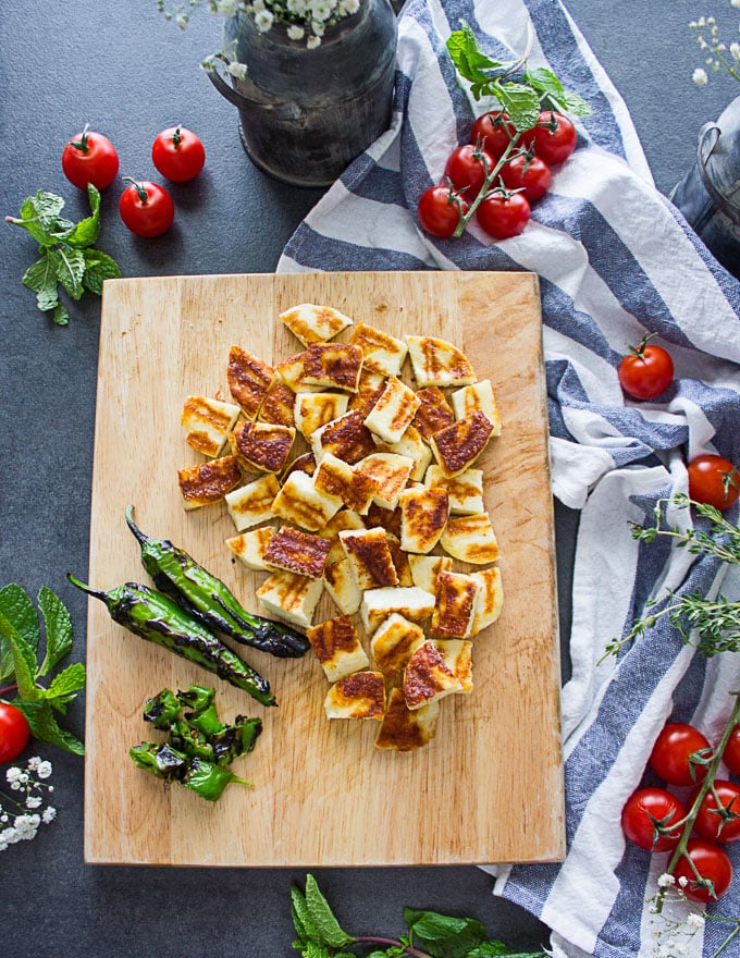 A cutting board with the grilled chopped halloumi cheese and shitsito peppers