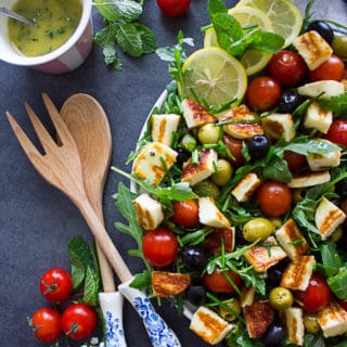 A half plate of salad showing the wooden spoons and tomatoes on the side