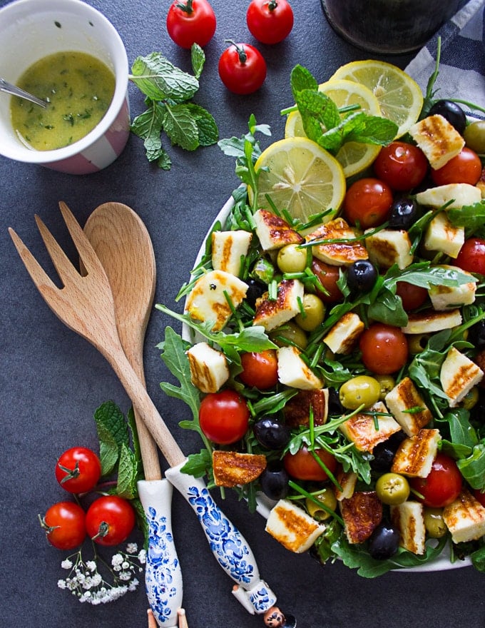 A half plate of salad showing the wooden spoons and tomatoes on the side