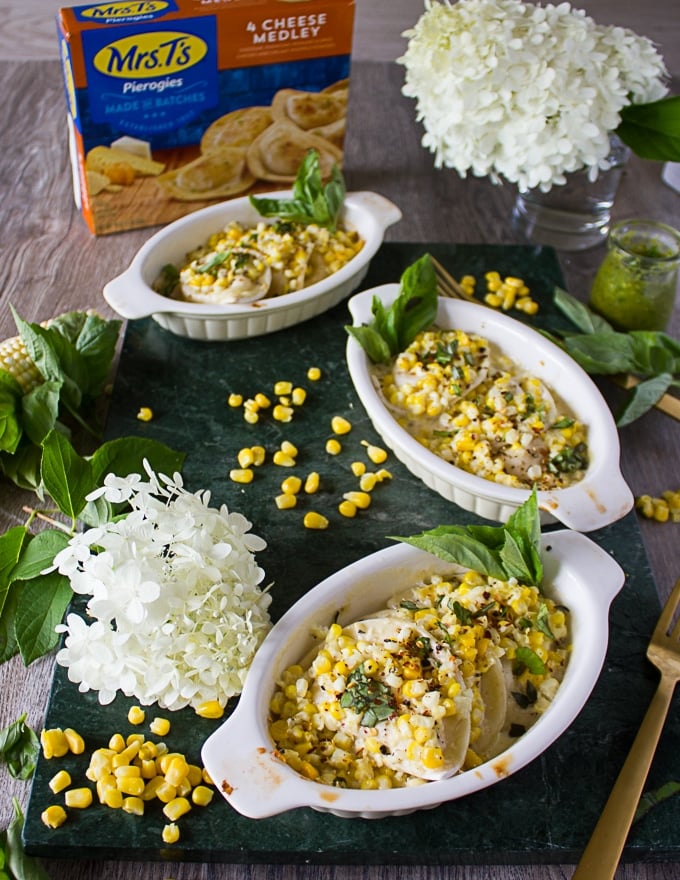 4 ramekins with corn casserole made using pierogies on a marble board surrounded by corn kernels, fresh basil and a box of pierogies