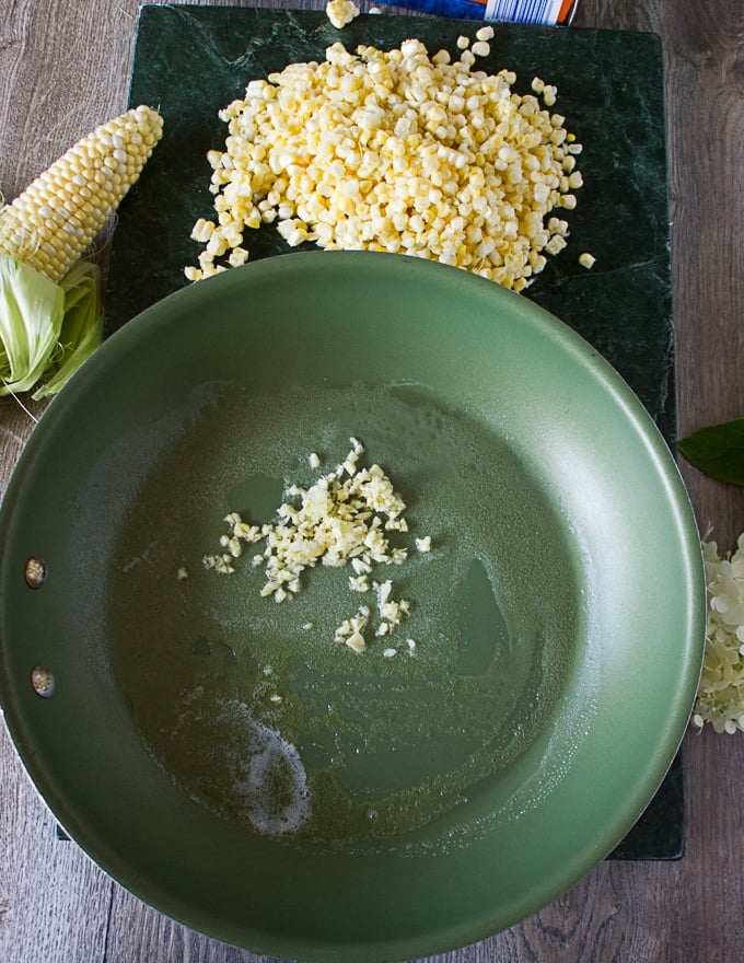 A pan sauteeing garlic and butter with the corn kernels on the side ready to cook