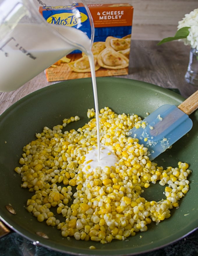 Corn kernels cooking in the garlic butter skillet and cream being added over it 