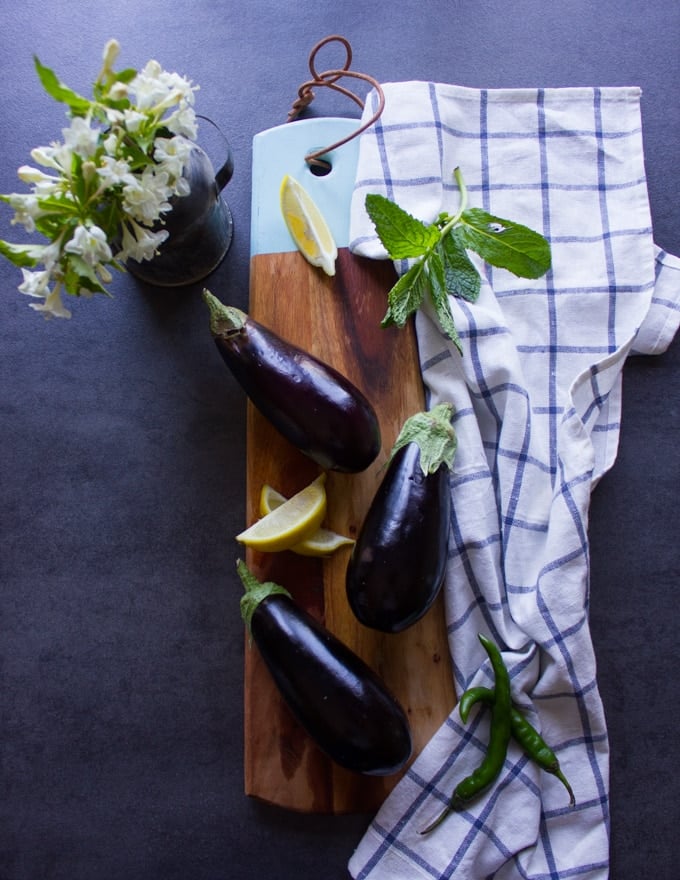 small egplants on a cutting board surrounded by a tea towel and white flowers in a cup