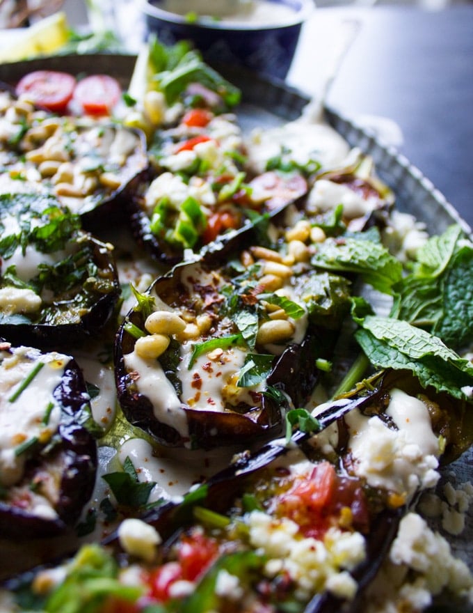 Side view of a fried eggplant half topped with tahini, pine nuts and surrounded by lots of fresh mint