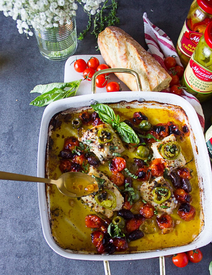 baked fish out of the ovena nd a spoon drizzling the olive oil over the fish