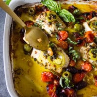 A spoon drizzling the juices and olive oil over the baked fish