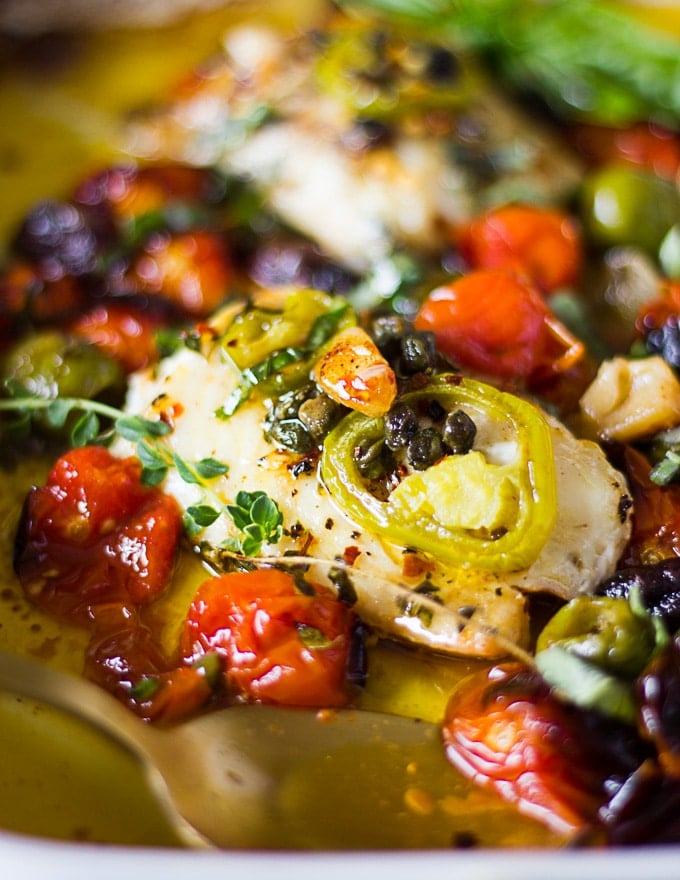 Close up of the baked fish surrounded by olives and tomatoes, topped with capers and jalapenos