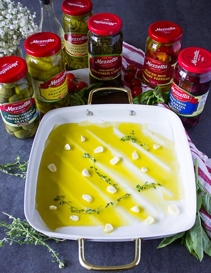 An oven pan with olive oil and sliced garlic and fresh thyme