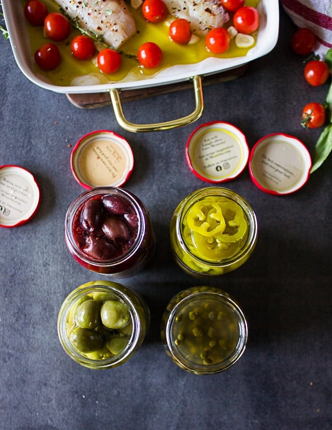 Opened up jars of olives and sliced jalapenos and capers for topping the fish 