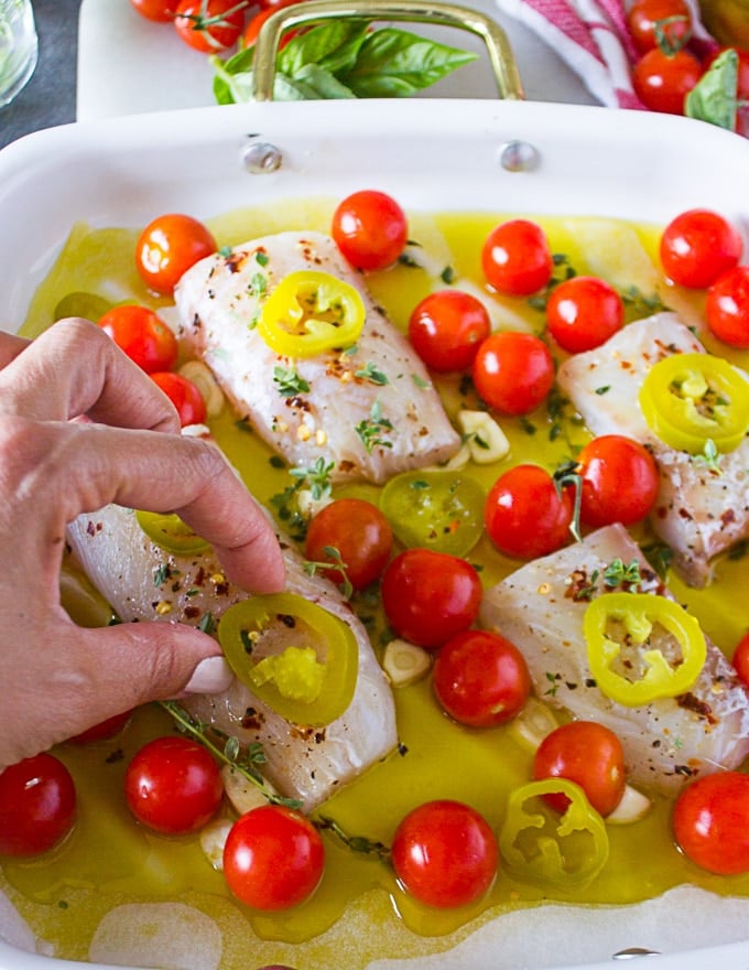 A hand placing the jalapenos over the fish