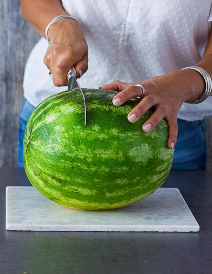 A hand holding a whole watermelon and slicing it into discs