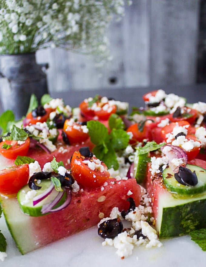 close up of one watermelon salad cut into wedge topped with onions, tomatoes, feta, olives and mint