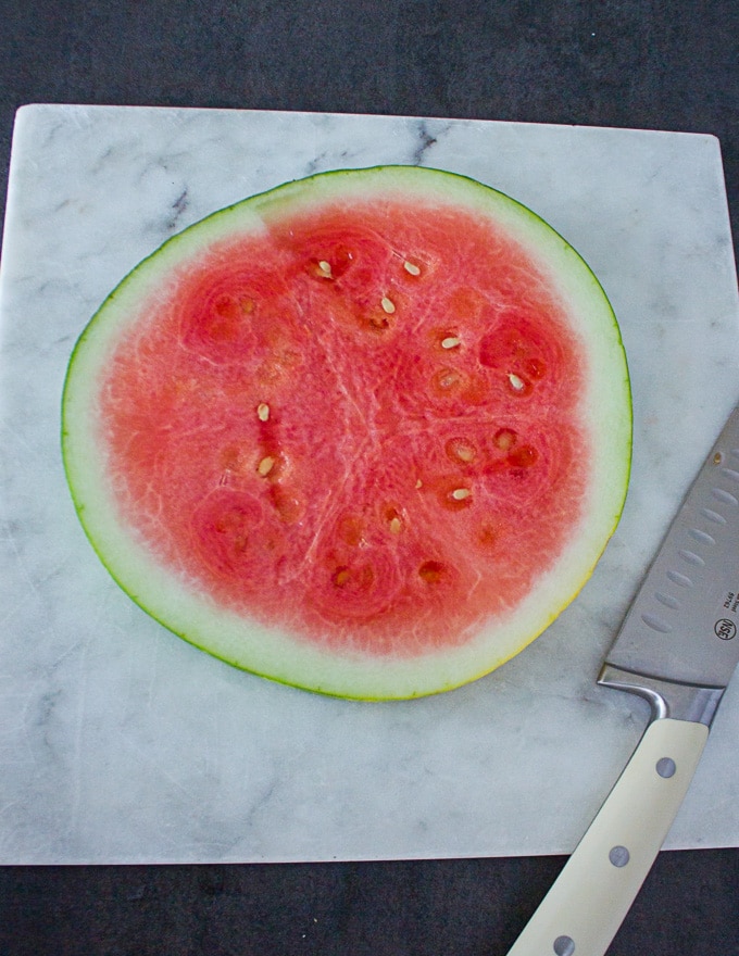 A slice or disc of watermelon cut up on a white marble and a white knife ready to cut up the watermelon into wedges