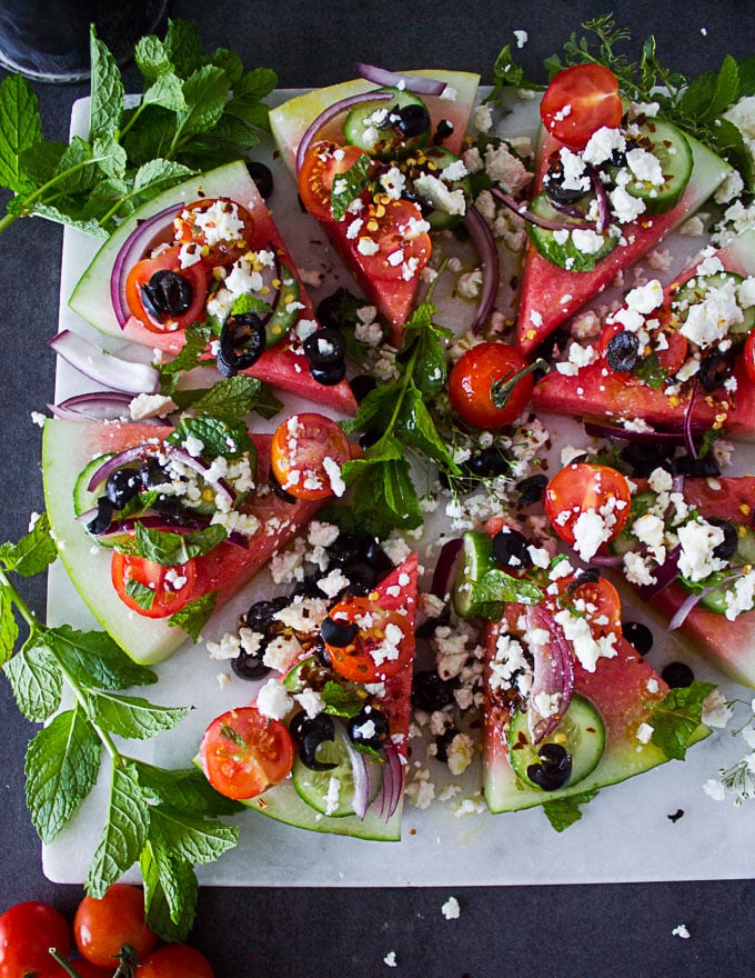 A whole disc of watermelon cut up into wedges and loaded with Greek salad toppings