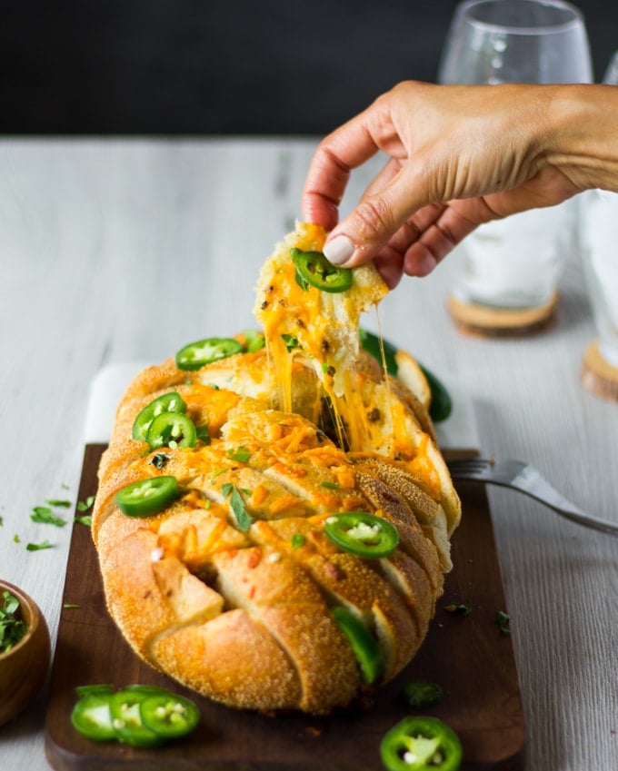 A hand pulling a chunk of the pull apart bread showing the stretchy cheese