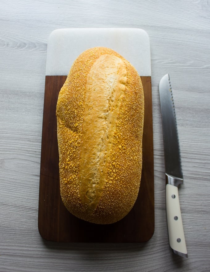 A whole loaf of soft Itlain bread on a cutting board and a serrated knife on the side