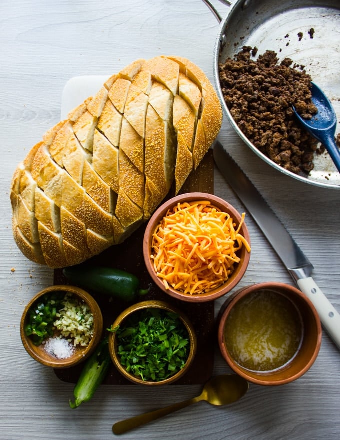 Ingredients for the pull apart bread recipe. A sliced loaf of bread, lamb crumbles, shredded cheese, melted butter, garlic, jalaoeno and salt