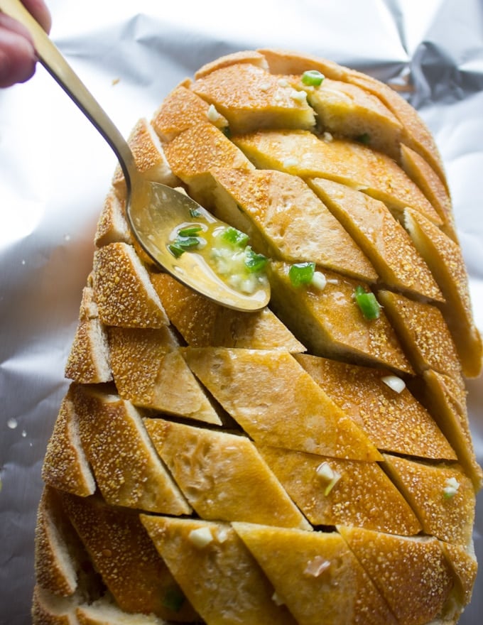 A spoon drizzling off the butter mixture along the diagonal slits on the bread loaf