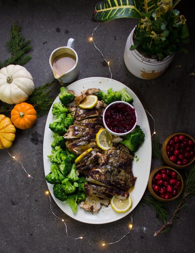 Top view of the table set up showing the plate of turkey breast, sliced and served with sauce. Some small pumpkins on the side, some bowls of cranberries, a gravy boat and some lights around.