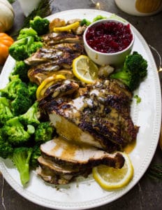 turkey berast recipe, sliced and drizzled with gravy showing one slice in a serving plate with broccoli and lemon slices