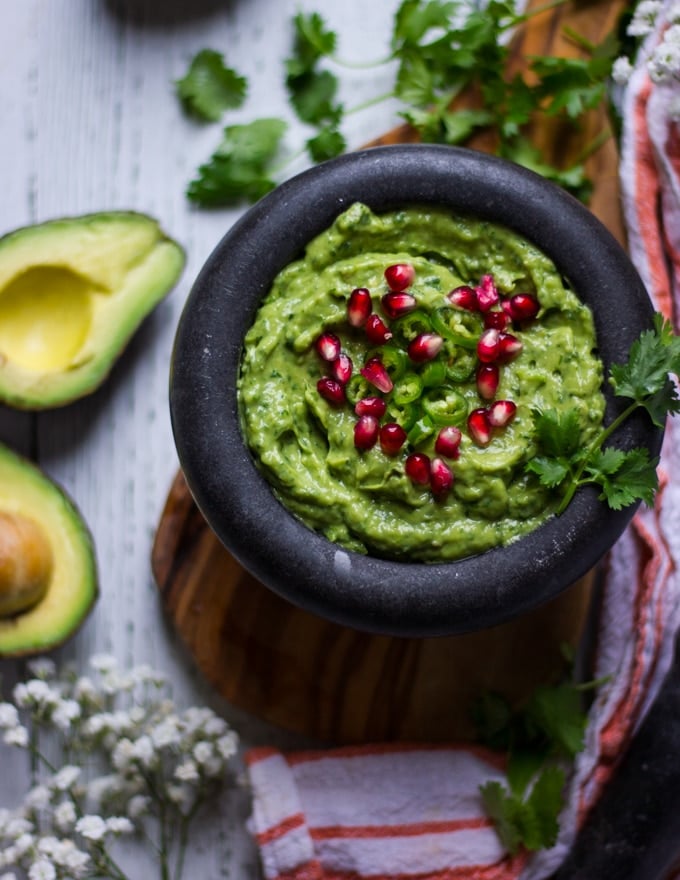 A close up of finished easy guacamole recipe over a wooden board topped with cilantro, jalapeno and ready to serve 