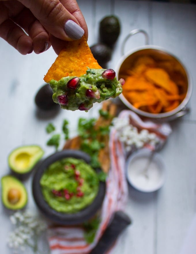 A hand holding a chip dipped in guacamole and close up of the guacamole dip over the chips 