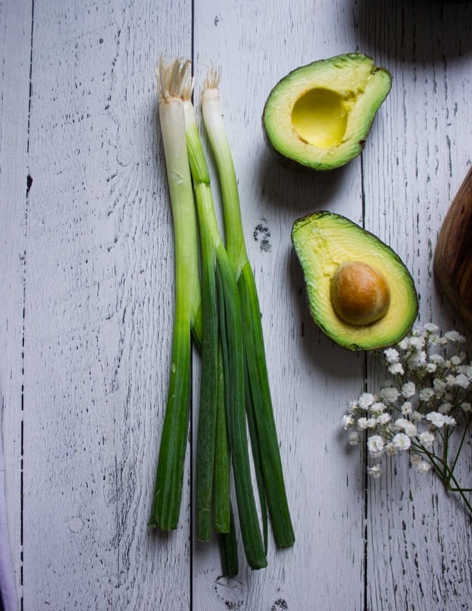 Scallions on a white board surrounded by avocados