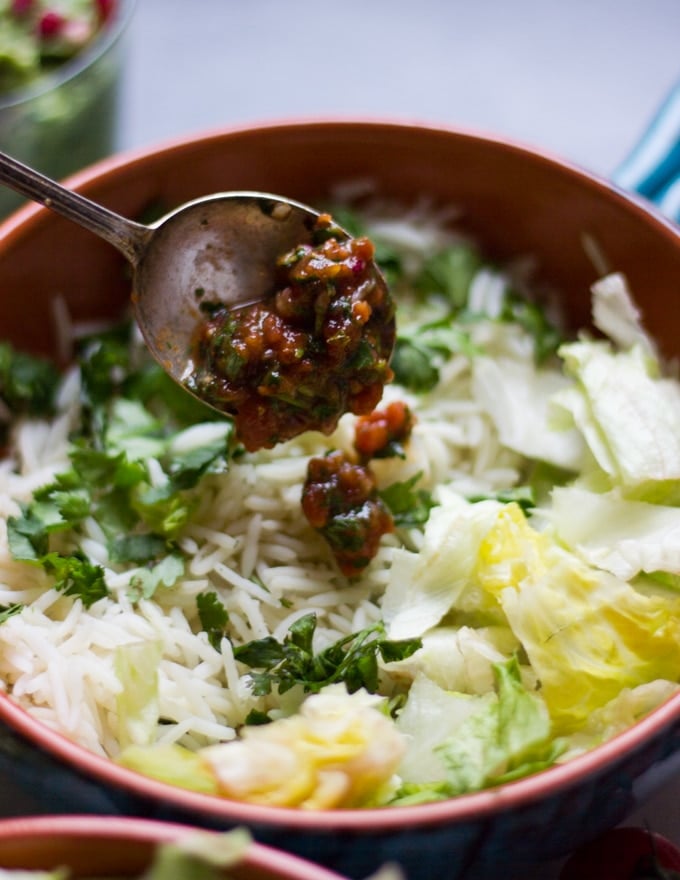 A spoon adding salsa over the base of the bowls of rice and lettuce