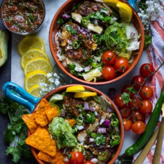 2 ready fajita bowls assembled with the toppings like guacamole, salsa, onion, tomatoes, jalapeno, surrunded by lemon slices, cilantro