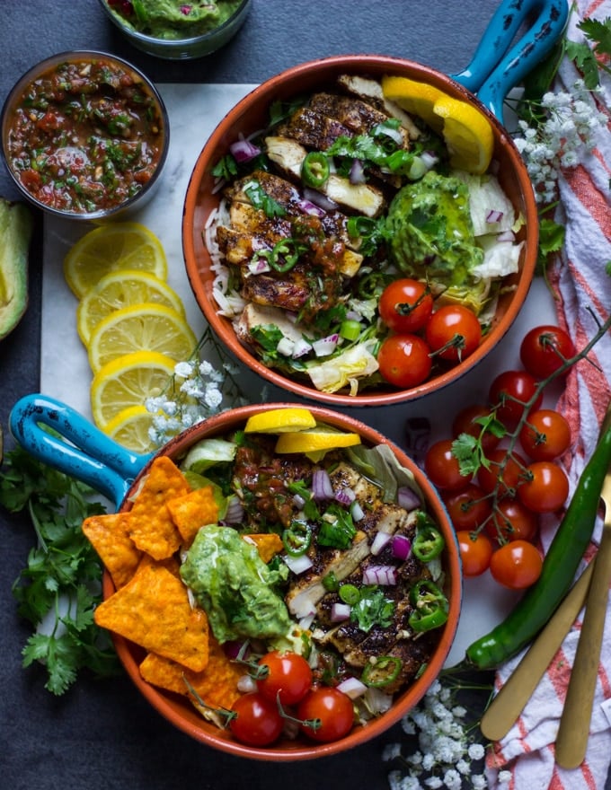 2 ready fajita bowls assembled with the toppings like guacamole, salsa, onion, tomatoes, jalapeno, surrunded by lemon slices, cilantro 