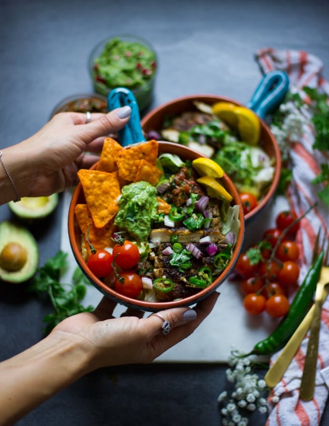 A hand holding a fajita bowl loaded with tomatoes, chips, salsa, guacamole and chicken