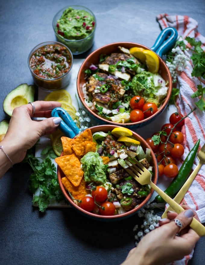 A hand holding a fork and trying to eat one of the fajita bowls using a fork