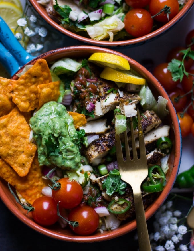 One bowl of chicken fajitas loaded with chips, chicken, guacamole, lime slices and a fork over the chicken 